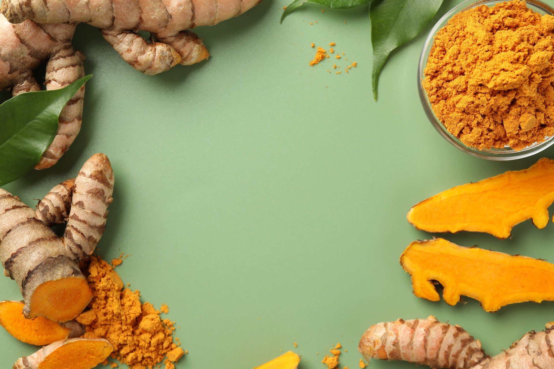 Frame of aromatic turmeric powder, raw roots and leaves on green background, flat lay