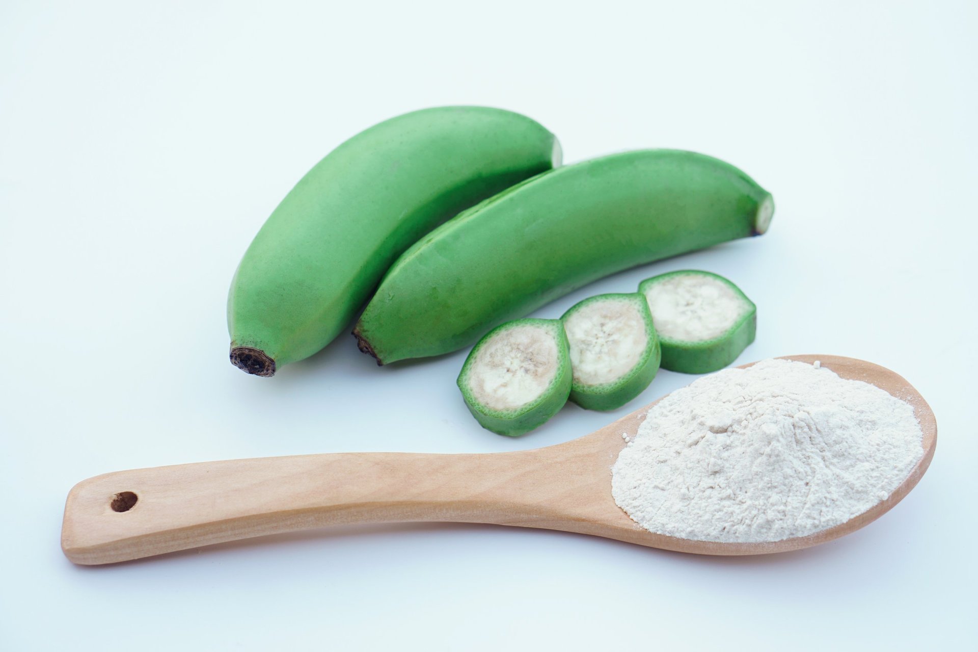 Green bananas and banana flour on wooden spoon, natural gluten-free alternative
