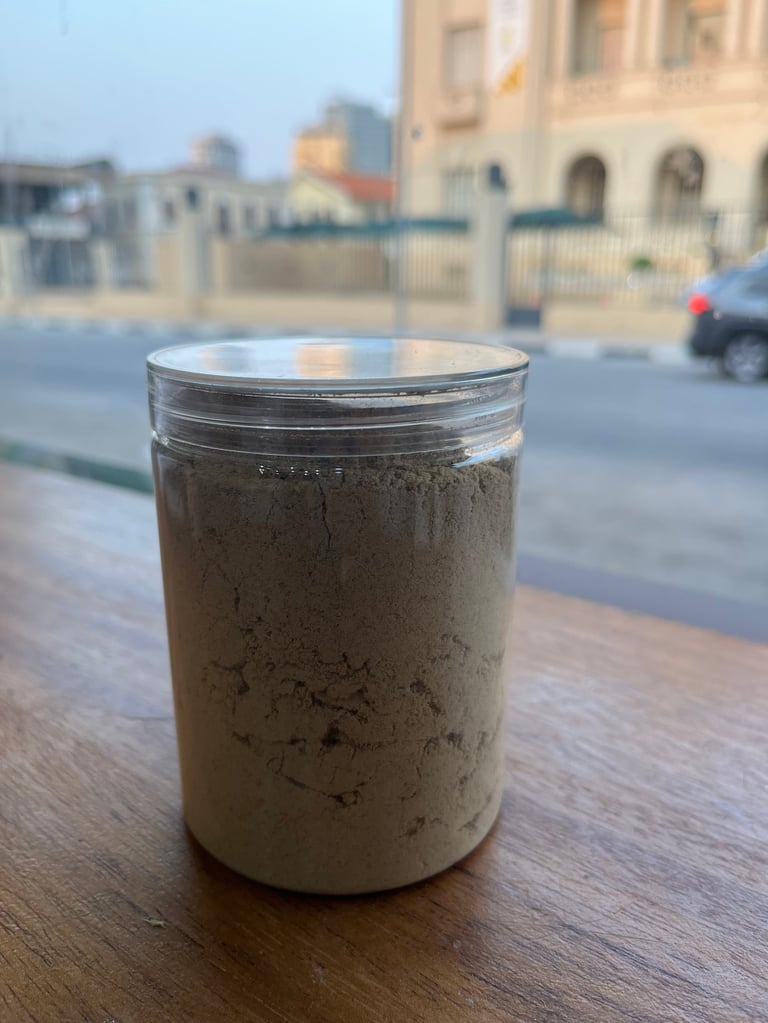 Clear glass jar with tan-colored paste or mixture on wooden table outdoors, buildings visible in blurred background
