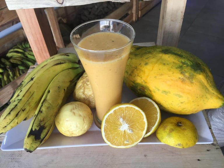 Glass of fresh citrus juice surrounded by papayas, bananas, oranges, and other tropical fruits on a white plate