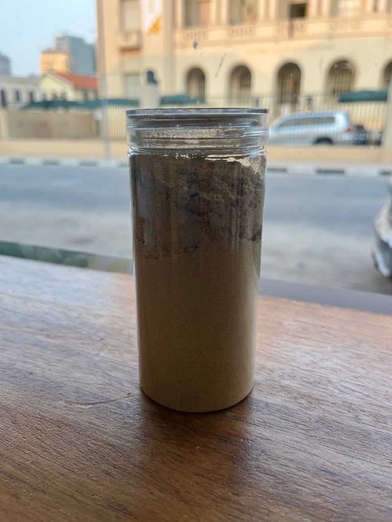 Clear glass jar of dark iced coffee on a wooden table with a street and beige buildings blurred in the background