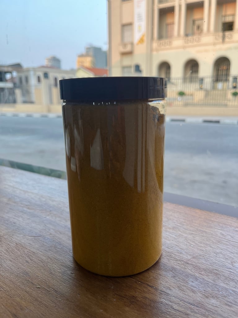 Glass jar with black lid containing brown honey or paste on wooden table with coastal buildings in background