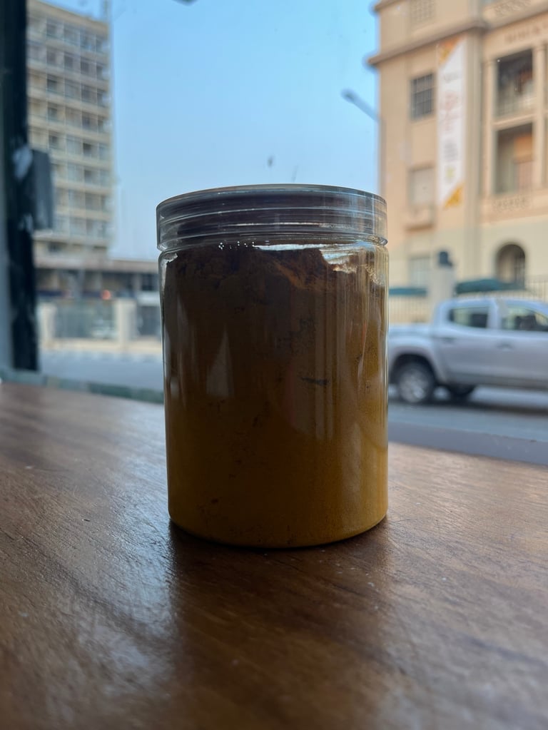 Glass jar of brown paste or spread sitting on a wooden table outdoors with urban street and buildings in background